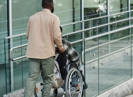 Photo of a man pushing a person in a wheelchair up a ramp